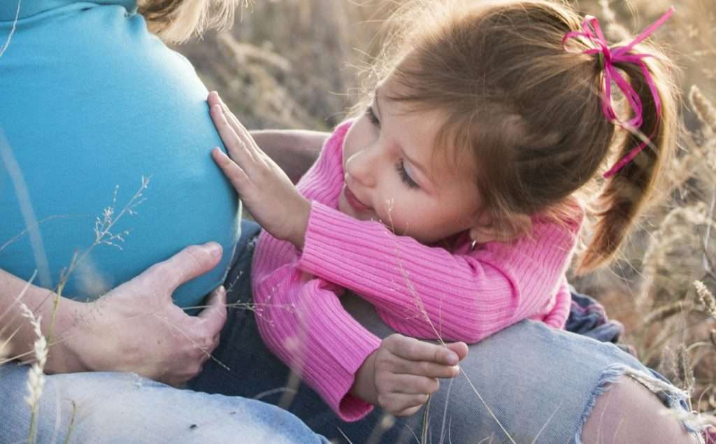Little girl touching pregnant belly.